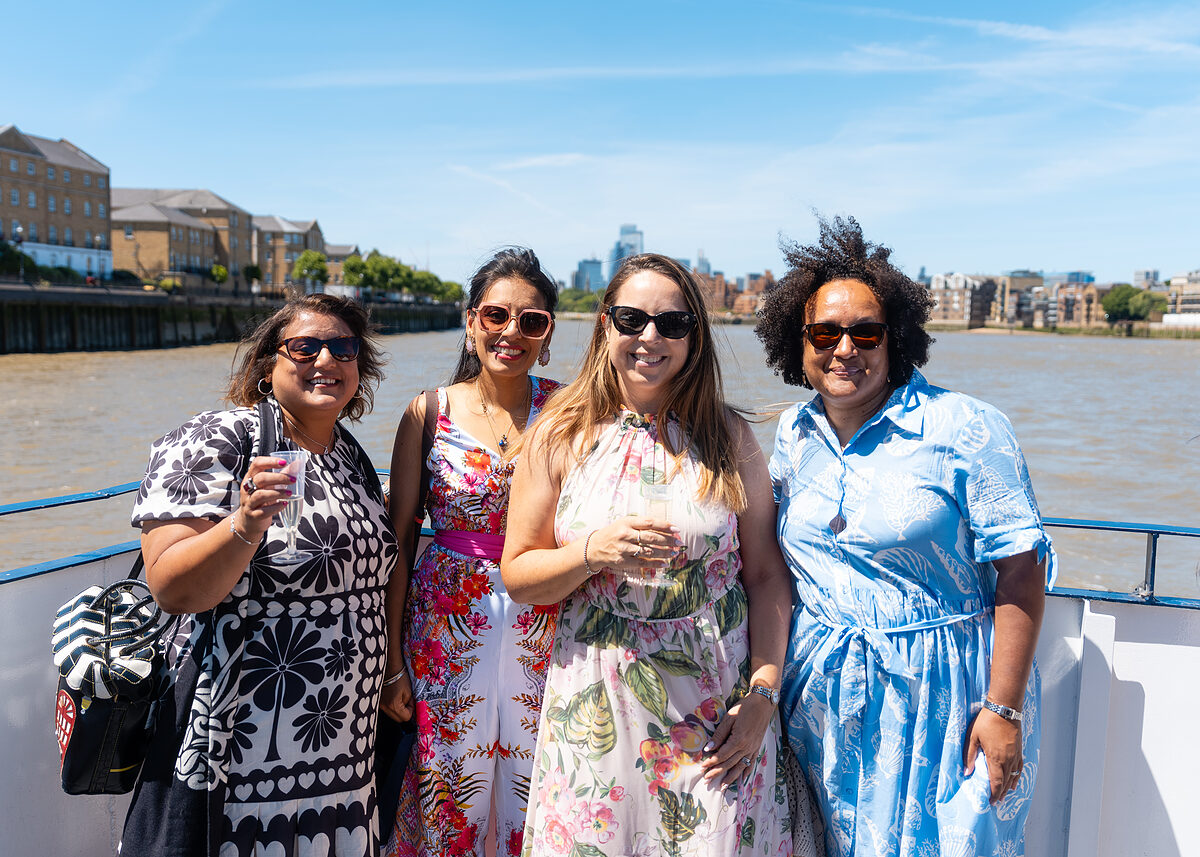 Four smiling members of the f:Entrepreneur community with drinks on the deck of a boat on the Thames