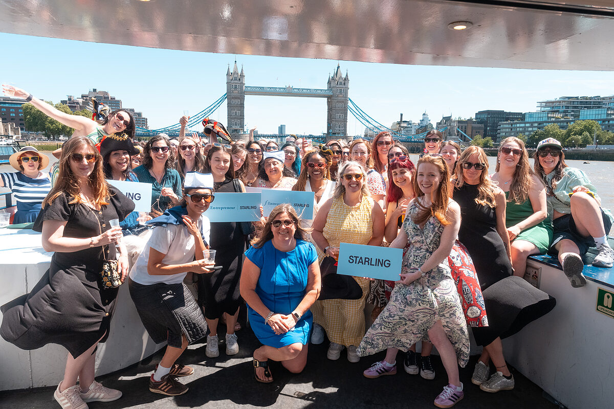 A large group photo of the Female Founders List community on the deck of a boat, with Tower Bridge behind them